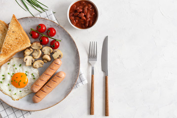 Traditional English Breakfast: sausages, grilled tomatoes and mushrooms, egg, baked beans and bread on the plate on white background. Top view, copy space. Menu concept