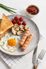 Traditional English Breakfast: sausages, grilled tomatoes and mushrooms, egg, baked beans and bread on the plate on white background. Top view. Menu concept