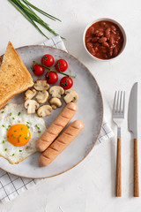 Full English Breakfast including sausages, grilled tomatoes and mushrooms, egg, baked beans and bread. Top view
