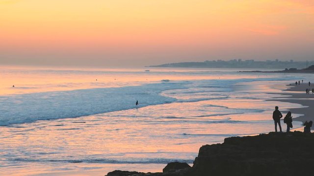 Incredible beautiful sunset sky reflections of atlantic ocean waves at Carcavelos beach near Lisbon, amazing orange teal and blue tones, man walking.