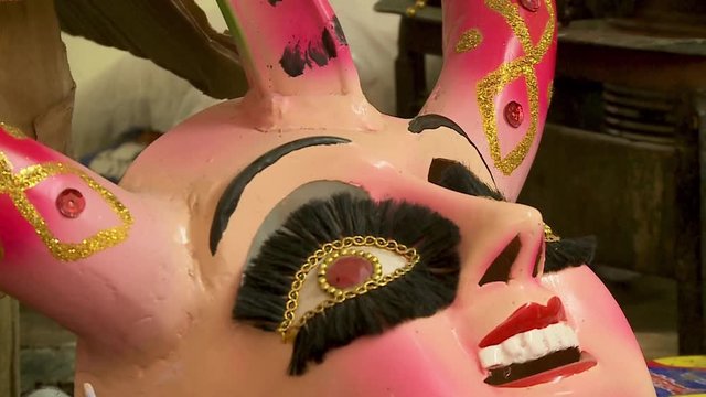 Extreme close-up low-angle tilting shot of a colourfully painted female devil mask, China Supay, displayed at an artisan's workshop, Oruro, Bolivia