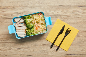 Top view of plastic lunch box with risotto, chicken and broccoli on wooden table
