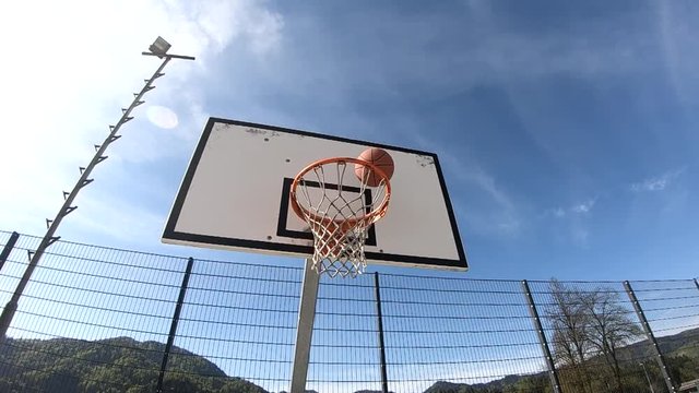 SLOWMO View of a basketball backboard with the ball hitting the hoop and bouncing off it on a sunny blue sky day.
