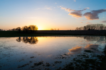 Fototapeta na wymiar The settting sun reflected in a pool of water during late winter in east flanders.