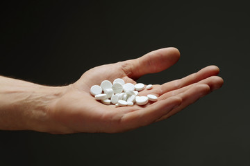A handful of pills in the male hand on a dark background.
