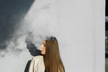 Vape teenager. Young cute girl in  casual clothes smokes an electronic cigarette near the wall...