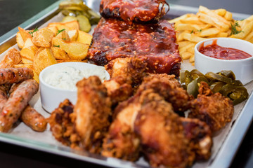 Dish of mixed meats. Grilled ribs, chicken wings and sausages with French fries