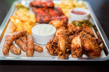 Dish of mixed meats. Grilled ribs, chicken wings and sausages with French fries