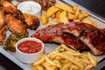 Dish of mixed meats. Grilled ribs, chicken wings and sausages with French fries