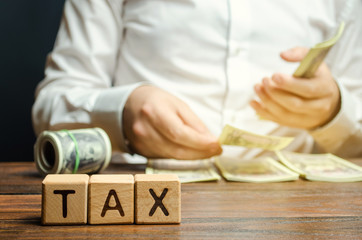 Wooden blocks with the word Tax and a businessman who counts money. The concept of time payment of taxes. Tax rates. Taxation / burden. Pay off debts. Property taxes