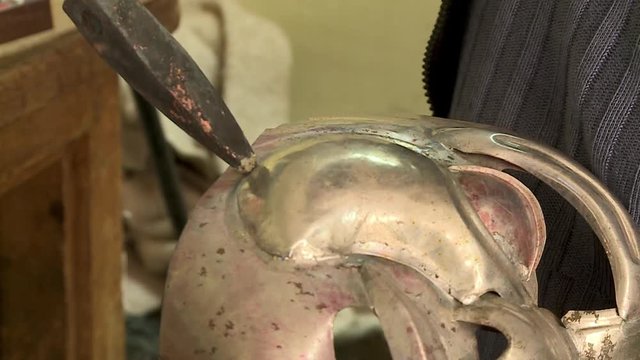 Extreme close-up low-angle still shot of a tinsmith soldering a carnival mask's chin at a local workshop, Oruro, Bolivia