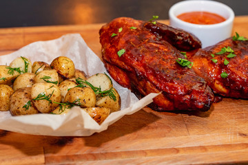 Smoked chicken thights served with potato and sauce on wooden tray close