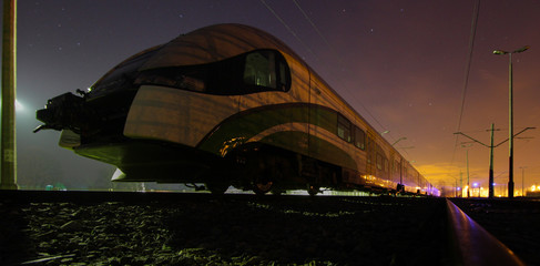 A suburban train standing at night on a siding.