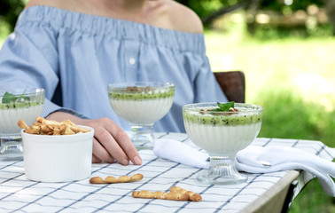 Girl at the garden table with a white tablecloth eats a kiwi milk dessert. Breakfast outdoors.