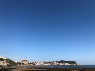 Fototapeta na wymiar View across beach at low tide towards Scarborough town and castle on hill, under a clear blue sky on a sunny day 