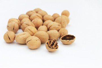 Whole and cracked walnuts on a white background, with a scattered shallow shell, in natural light.