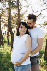 Fototapeta premium Pregnant woman and her beaeded husband hugging on the tummy together in nature outdoor