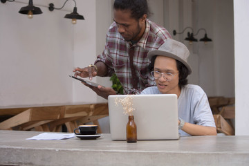 two young creative man discuss with laptop and tablet, young asian and black man working with tablet and laptop in a cafe, papua and asian man working together