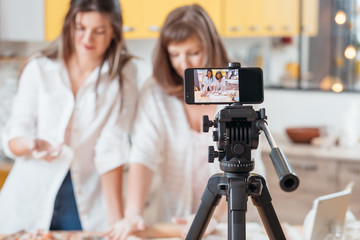 Culinary vlog. Two women baking shooting smartphone video tutorial. Content creating equipment. Online business hobby.