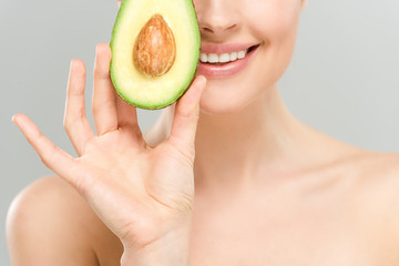 cropped view of naked smiling woman holding half of tasty avocado isolated on grey