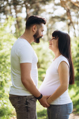 Fototapeta premium Pregnant woman and her beaeded husband hugging on the tummy together in nature outdoor