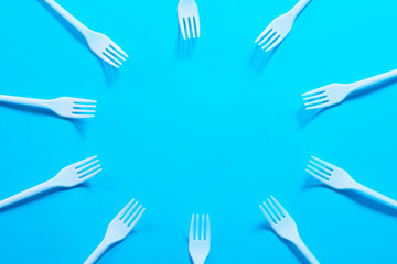 Air pollution. Plastic littering. Ecology problem. White disposable forks creating circle frame on sky blue background. Copy space.