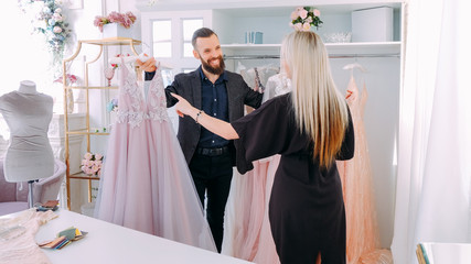 Luxury showroom. Fashion consultant showing elegant evening gown to female client.