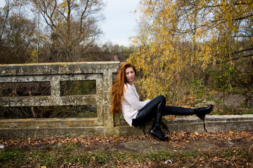 Portrait of young redhead woman sitting on a bench in autumn park