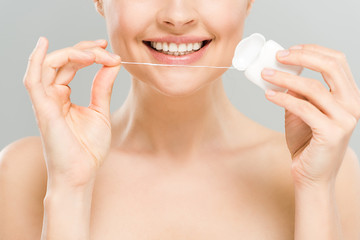 cropped view of cheerful naked woman holding dental floss near teeth isolated on grey