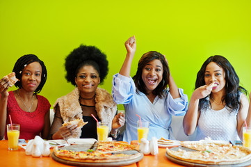 Four young african girls in bright colored restaurant eating pizza and having fun together.