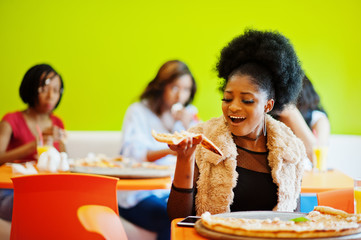 African woman with pizza sitting at restaurant against dark skinned girls.