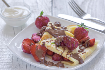 Pancakes with strawberries drizzled with chocolate. On a white wooden background.