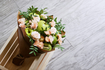 Bouquet of fruits and flowers. Asian pear, green apple, kiwi fruit, avocado, beige rose, pistachio. Gray wooden background.