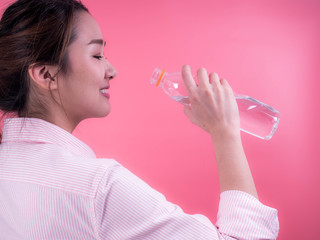 Beautiful asian young woman drinking a bottle of water isolated on a pink background.
