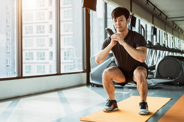 Sport man doing squat posture on yoga mat in fitness gym at condominium in urban. People lifestyles...