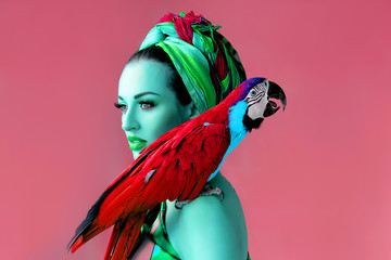 Ultraviolet portrait of young attractive woman in african style holding ara parrot on her hand on bright background © k8most
