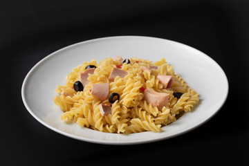 Pasta with tuna and tomatoes in a white plate on black