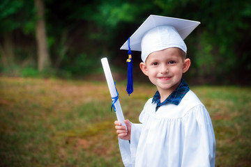 Cute smiling boy in cap and gown after kindergarten graduation