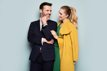 Joyful couple, elegantly dressed, standing on a blue background