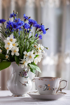 On the table is a cup of tea and a bouquet of wild flowers in a vase