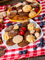 Oatmeal Cookies and sand chocolate cake with blueberries on wooden table with gingham cloth in farm style close up. Table setting breakfast for two with cups. Lunch in inexpensive cafe.