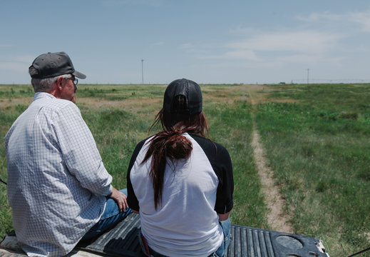father and daughter sit on tailgate of pickup in pasture