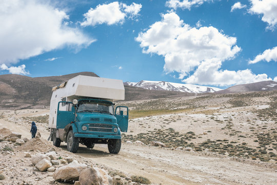 blue offroad camping truck on bad roads on the pamir highway with snowcovered mountains in the back