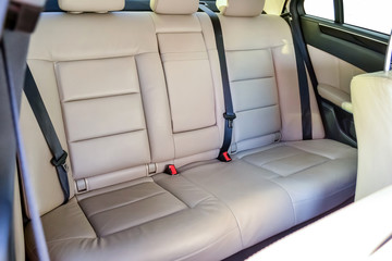 The rear seats of the car in the sedan body are white leather upholstered with the armrest folded down after dry cleaning and washing in a car repair shop. Auto service industry.