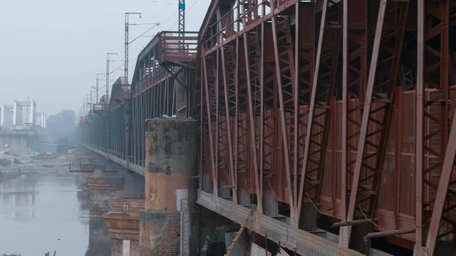 Gloomy metal girder bridge over the Yamuna river with heavy traffic of cars motorcycle, scooters and rickshaws in Delhi, India. Above the river strong smog. Shot in motion