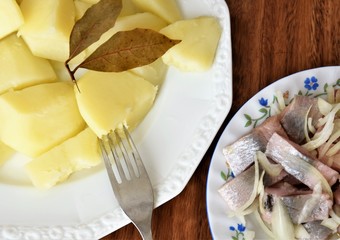 boiled peeled potatoes with bay leaves and slices of herring fish fillet with onions