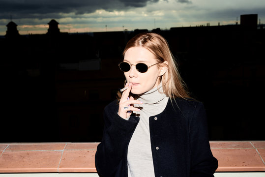 Elegant blonde woman in sunglasses smoking a cigarette on the ro