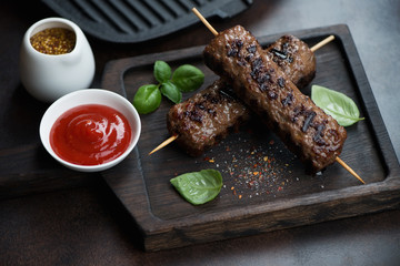 Wooden serving tray with grilled kebabs made of marbled beef meat, dipping sauce and dijon mustard, studio shot