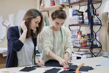 Seamstresses measure the fabric for sewing a dress in the atelier. Two female tailor working in in...