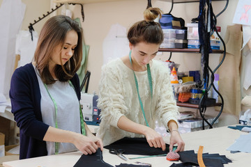 Seamstresses measure the fabric for sewing a dress in the atelier. Two female tailor working in in the sewing workshop.